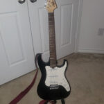 Lyon by Washburn Strat style electric guitar in player's lap, showcasing its sunburst finish and classic body shape