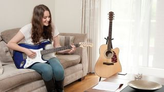 Woman playing electric guitar with acoustic guitar in background