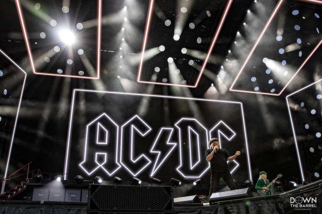 Angus Young of AC/DC performing a guitar solo on stage, center stage spotlight.