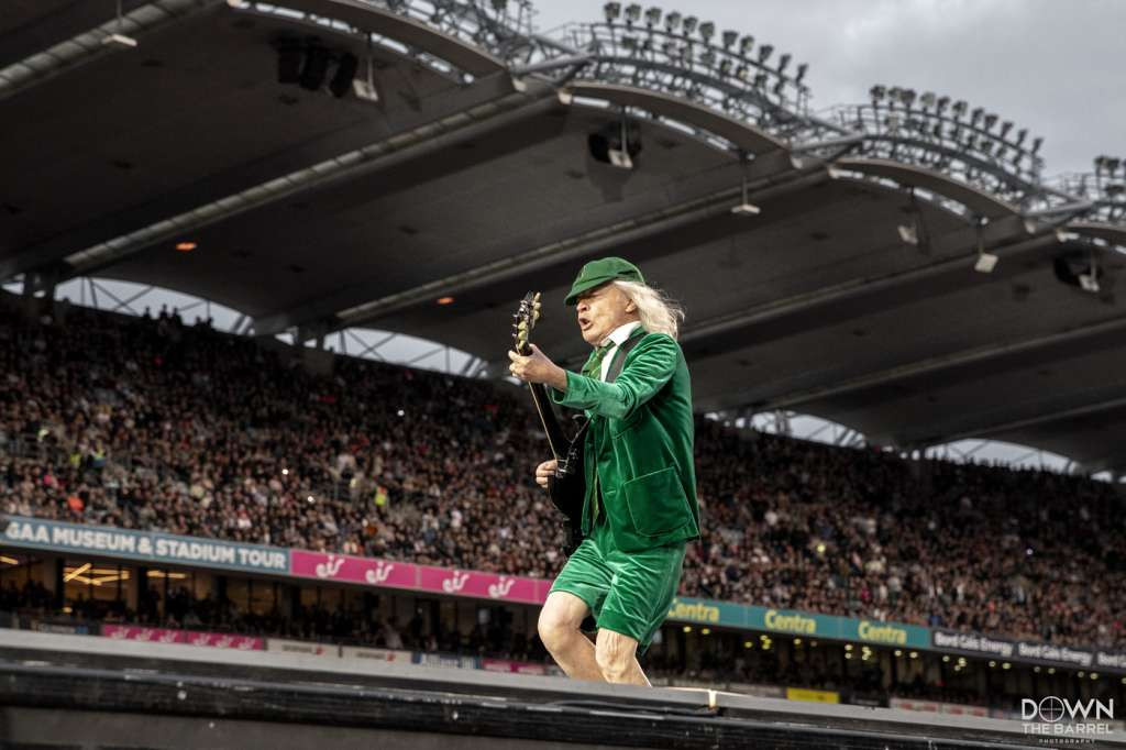 Brian Johnson of AC/DC singing on stage with Angus Young in the background.