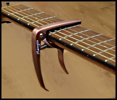 Adagio Pro Deluxe capo on a guitar neck, showcasing its spring-loaded mechanism and peg-puller feature.