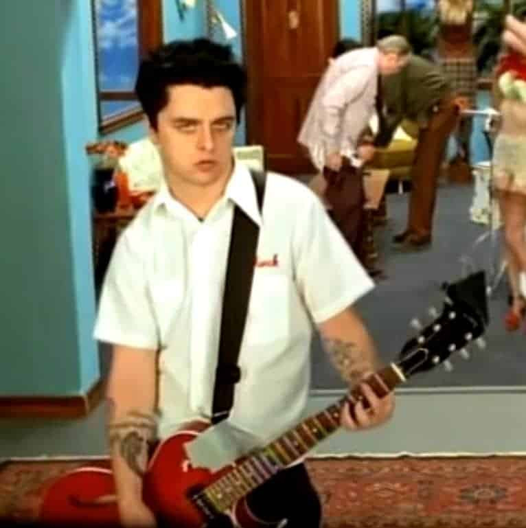 Billie Joe Armstrong playing a red Gibson ES-135 guitar in the &quot;Redundant&quot; music video, highlighting his use of semi-hollow guitars.
