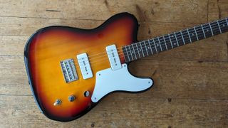 Angled shot of a sunburst Squier Paranormal Baritone Cabronita Telecaster electric guitar lying on a wooden floor