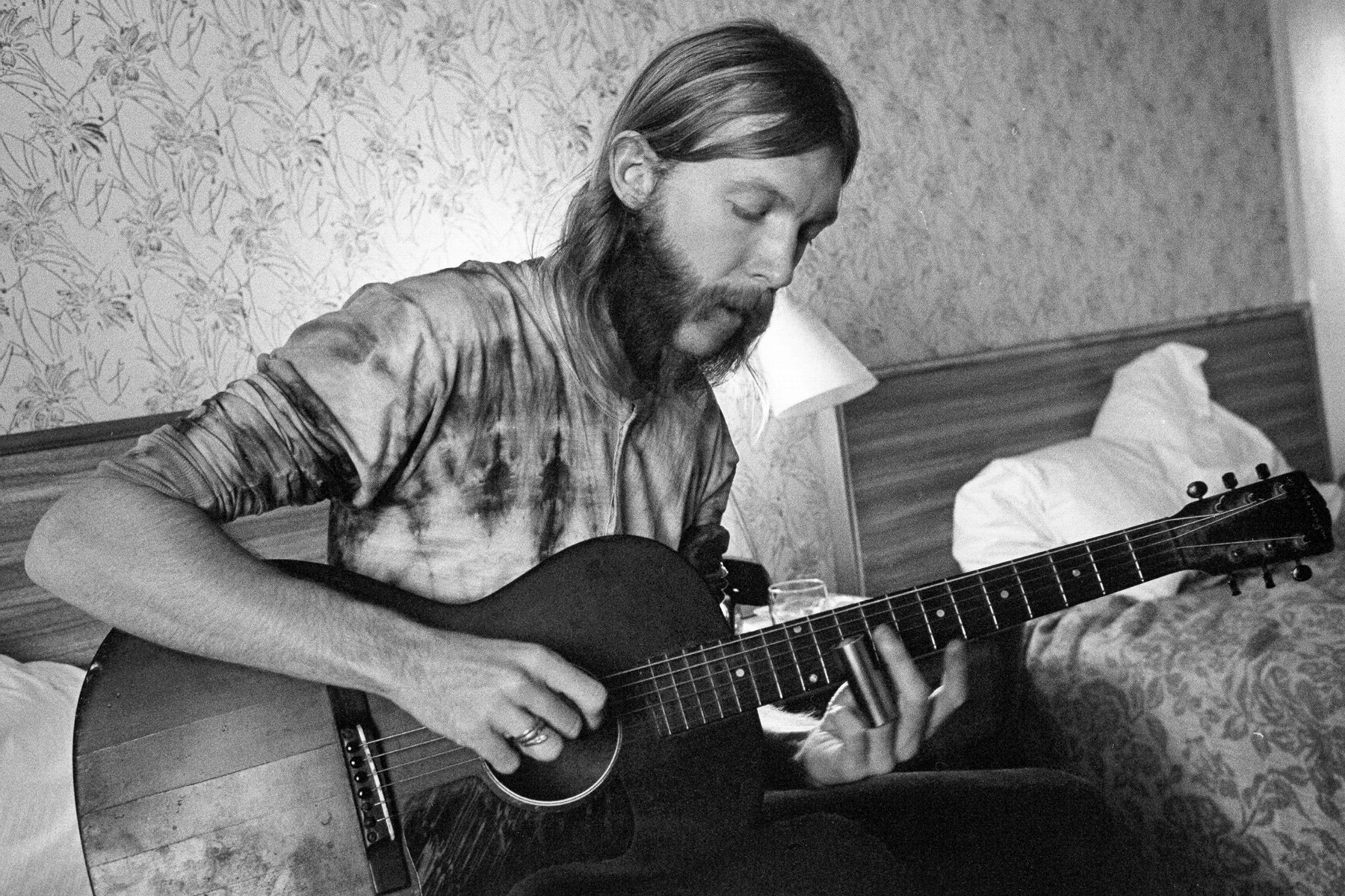 Duane Allman playing slide guitar in a hotel room, showcasing his visionary slide guitar style and his influence on Southern rock