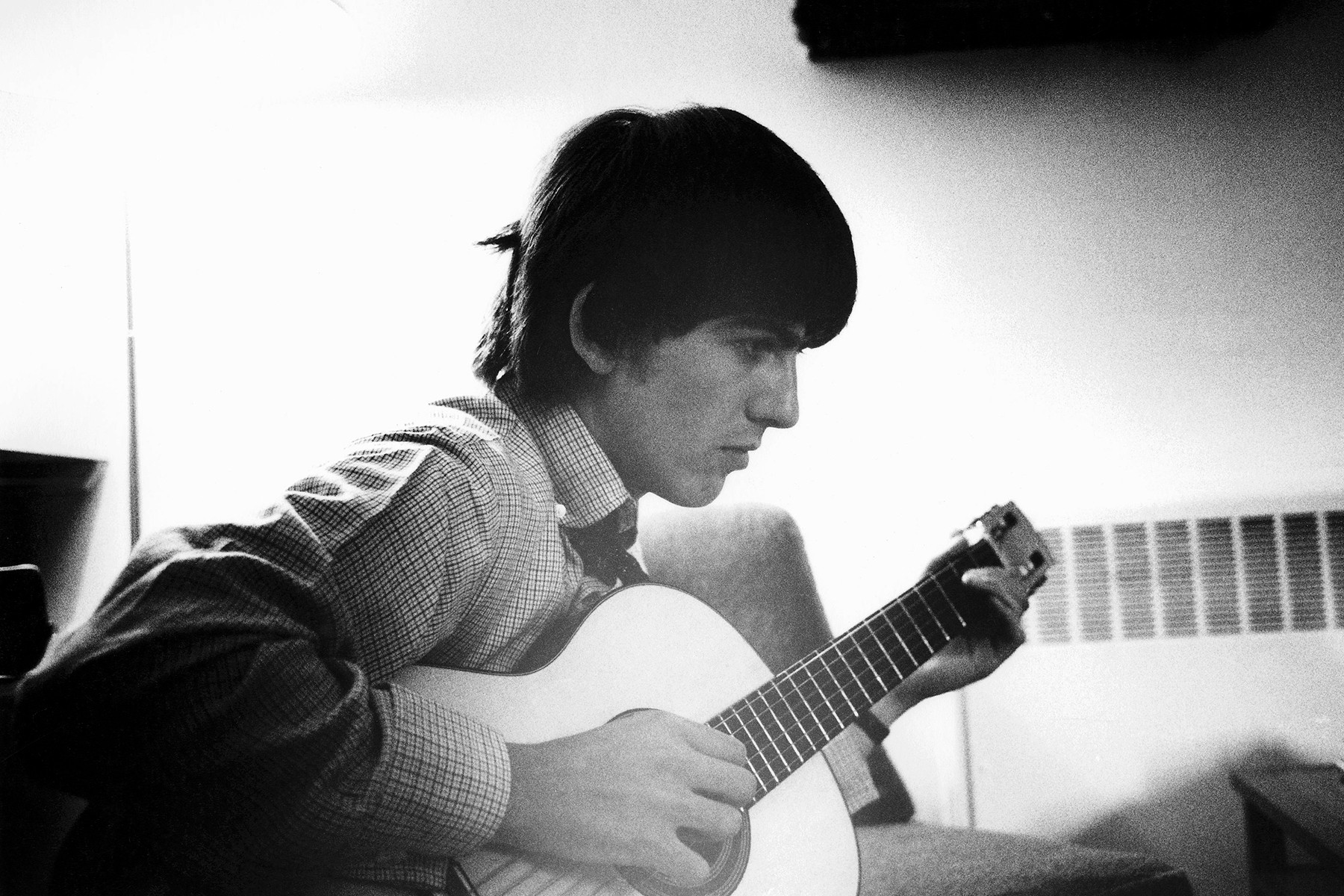George Harrison of The Beatles playing acoustic guitar at Twickenham Film Studios, showcasing his innovative guitar work within pop music