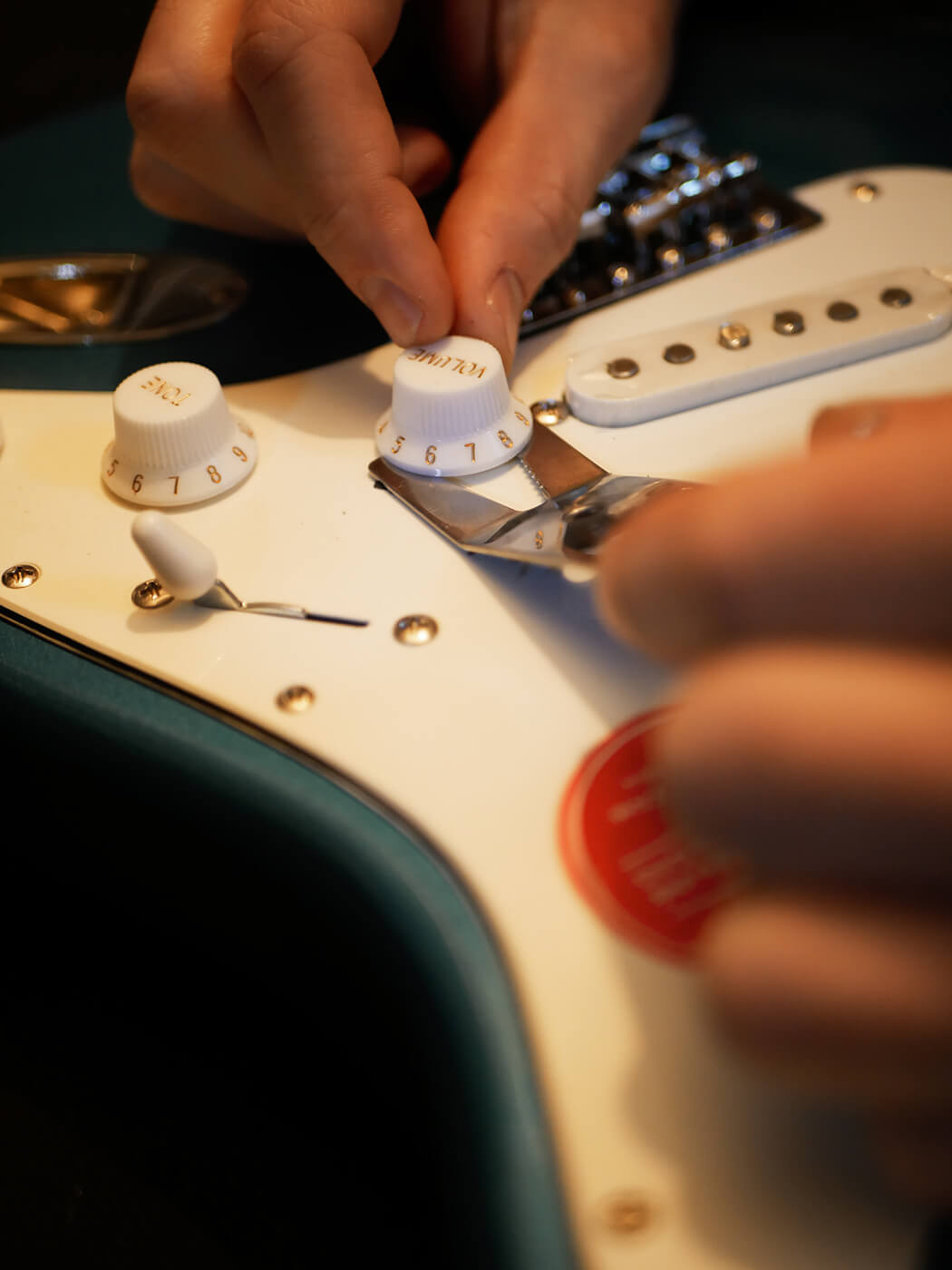 Hands using wire cutters to cut guitar strings during the removal process, demonstrating the first step in how to set up a guitar.
