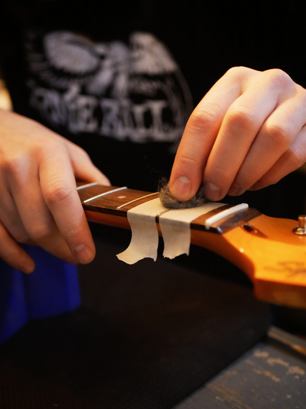 Hands using a wrench to gently remove a control knob from a guitar, illustrating the step of preparing the pickguard for cleaning during a guitar setup.
