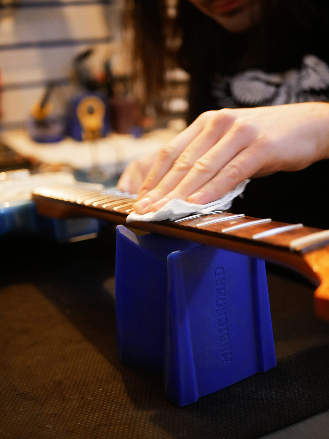 Hands gently rubbing steel wool along the guitar frets, demonstrating the fret polishing step in how to set up a guitar for smooth playability.