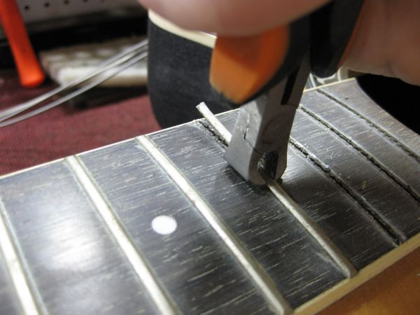 Frets partially removed from the bass fretboard, showcasing the initial stage of the defretting process