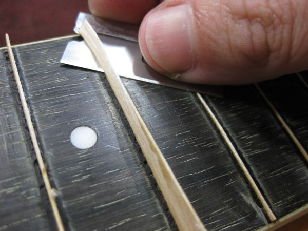Trimming the maple veneer fret lines flush with the rosewood fretboard using a razor blade