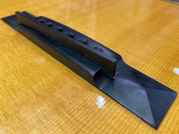 Ebony filler piece after being carved and sanded to match the guitar bridge