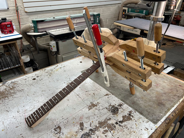 Cypress veneer being carefully applied to the guitar headstock, adding a visual and material connection to the guitar body.