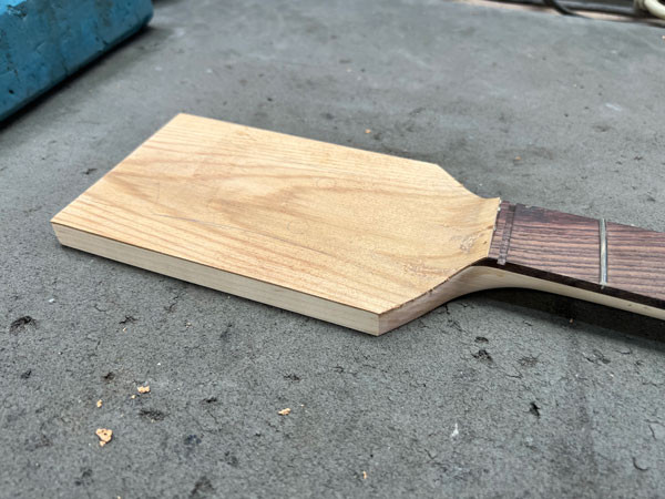 Headstock veneer application process, showing the cypress being shaped and adhered to the guitar neck headstock.