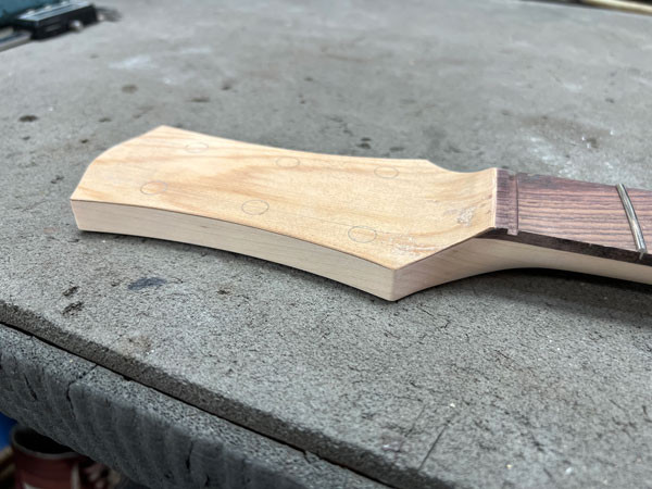 Shaped guitar headstock with the cypress veneer applied, showcasing a design that balances classic elements with unique features.