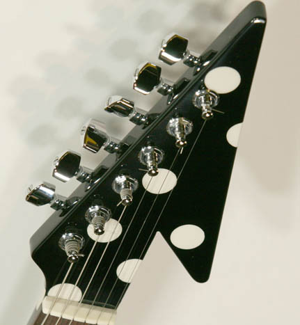 Detail view of the headstock of a Karl Sandoval Polka Dot Flying V guitar highlighting the tuners and logo