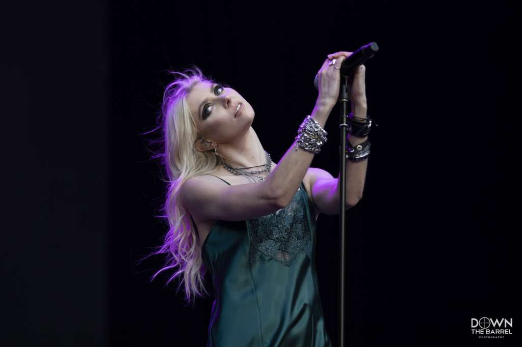 The Pretty Reckless band members performing on stage, bathed in red and white lighting.