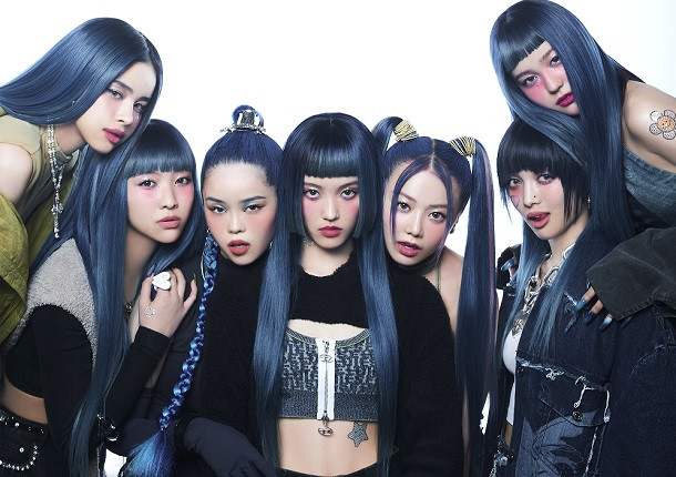 Kep1er members in colorful outfits, performing on stage with microphones.