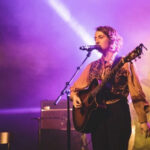 An artist deeply engaged in singing and playing guitar, bathed in stage light