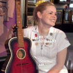 John Lennon's Gallotone 'Champion' acoustic guitar sits with restaurant waitress Jade Wilde at the announcement of the guitar's second auction by Sotheby's in London 24 August 1999 at the Hard Rock Cafe, a special piece of early Beatles memorabilia.