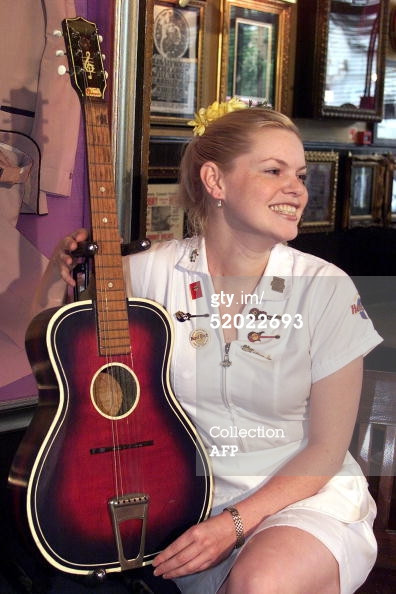 John Lennon's Gallotone 'Champion' acoustic guitar sits with restaurant waitress Jade Wilde at the announcement of the guitar's second auction by Sotheby's in London 24 August 1999 at the Hard Rock Cafe, a special piece of early Beatles memorabilia.